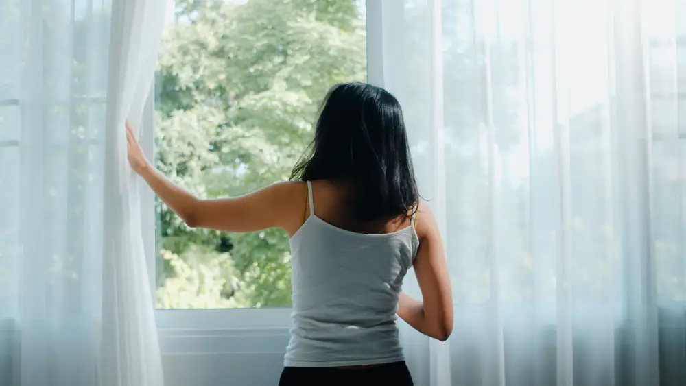 Happy beautiful Asian-woman-smiling-and-drinking-a-cup-of-coffee-or-tea-near-the-window- in-bedroom